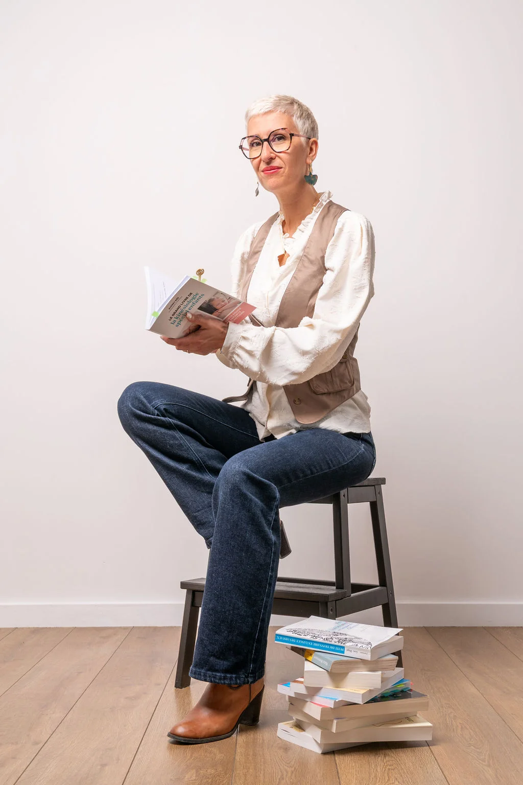 Christine Boury assise sur un tabouret avec sa collection de livre, lisant un livre
